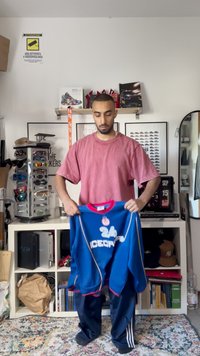 Modra atletska majica z rdečimi detajli, na kateri je natisnjeno "24" in "ICECATS". Model nosi črne trenirke v zmedeni sobi.