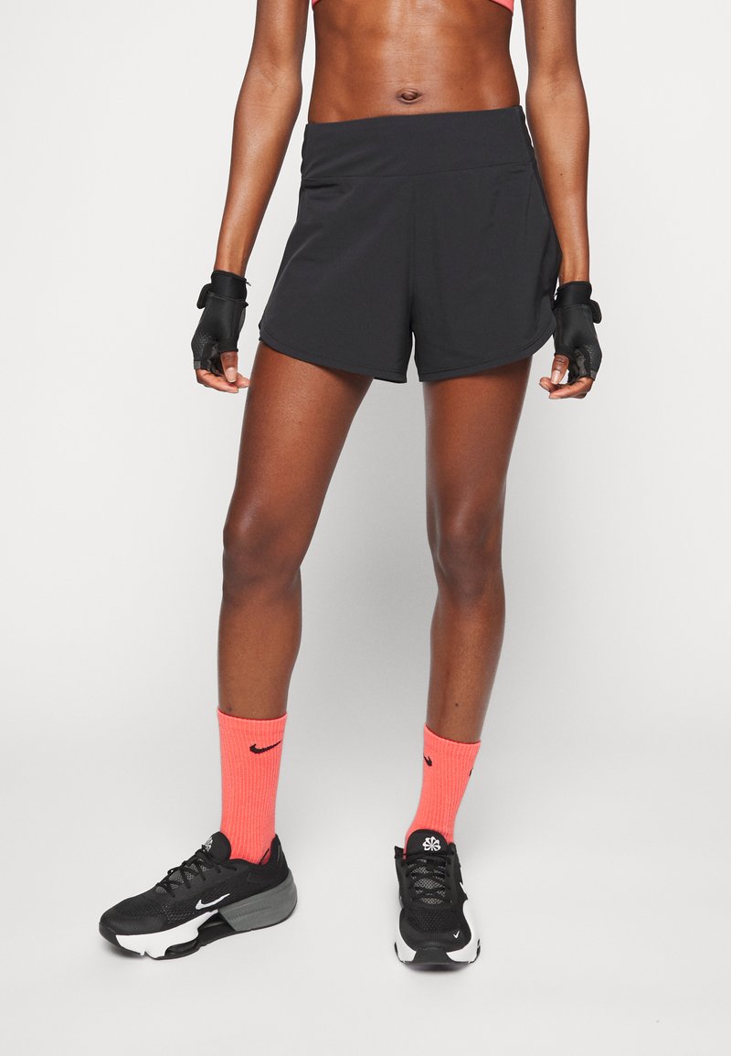 Pantaloni sportivi neri con una vestibilità comoda, abbinati a calzini rosa brillanti e sneakers nere. L'outfit presenta materiali testurizzati e nessun motivo visibile.