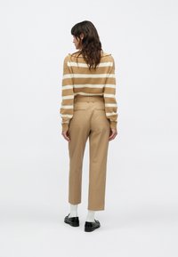 Džemper s prugama u boji nijanse smeđe i krem, uparen s bež hlačama. Hlače imaju ravni kroj i dva stražnja džepa. Crne cipele i bijele čarape.