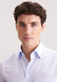 Jasnoniebieska i biała koszula w kratkę z kołnierzykiem zapinanym na guziki, z kieszonką na piersi i gładką bawełnianą teksturą.