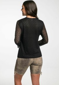 Zwarte lange mouw top met een diamanten kantpatroon en textuurstof, gecombineerd met beige shorts met zij-lacing details.