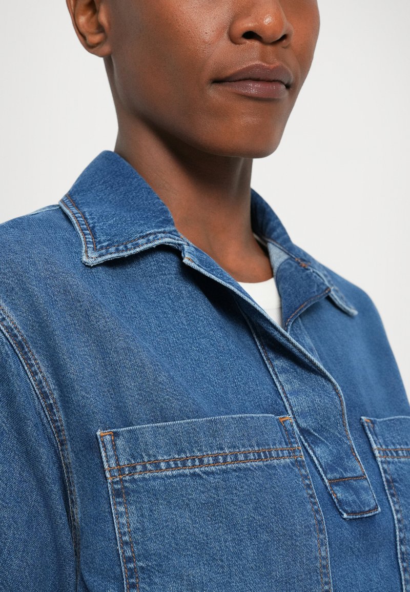 Jeansjacke in Hellblau mit einem kragenförmigen Ausschnitt, zwei Fronttaschen und sichtbaren Nähdetails. Der Stoff ist strukturiert und bequem.
