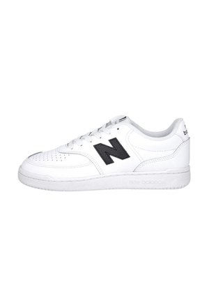 Zapatilla blanca New Balance con logo negro "N", diseño con cordones y perforaciones cerca de la puntera sobre fondo blanco.
