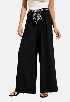 Svarta vida byxor med veck och ett zebra-mönstrat knytbälte, bärs med en vit topp och svarta sandaler med guldaccenter.