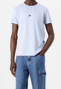 Světle modré bavlněné tričko s kulatým výstřihem, na kterém se nachází logo "Tommy Hilfiger" a "EST. 1985" v bílých a červených akcentů. Krátké rukávy.