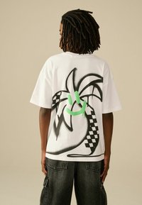 Weißes Baumwoll-T-Shirt mit einem sprühbedruckten grafischen Design eines lächelnden Gesichts mit grünen Akzenten und einem karierten Muster auf der unteren Seite.