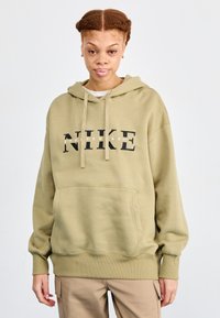 Alyvuogių žaliai spalvos džemperis su kapuce, priekine kengūrine kišenė ir juodu "NIKE SPORTSWEAR" logotipu. Minkšta, tekstūruota medžiaga su šonkaulinėmis rankovėmis.