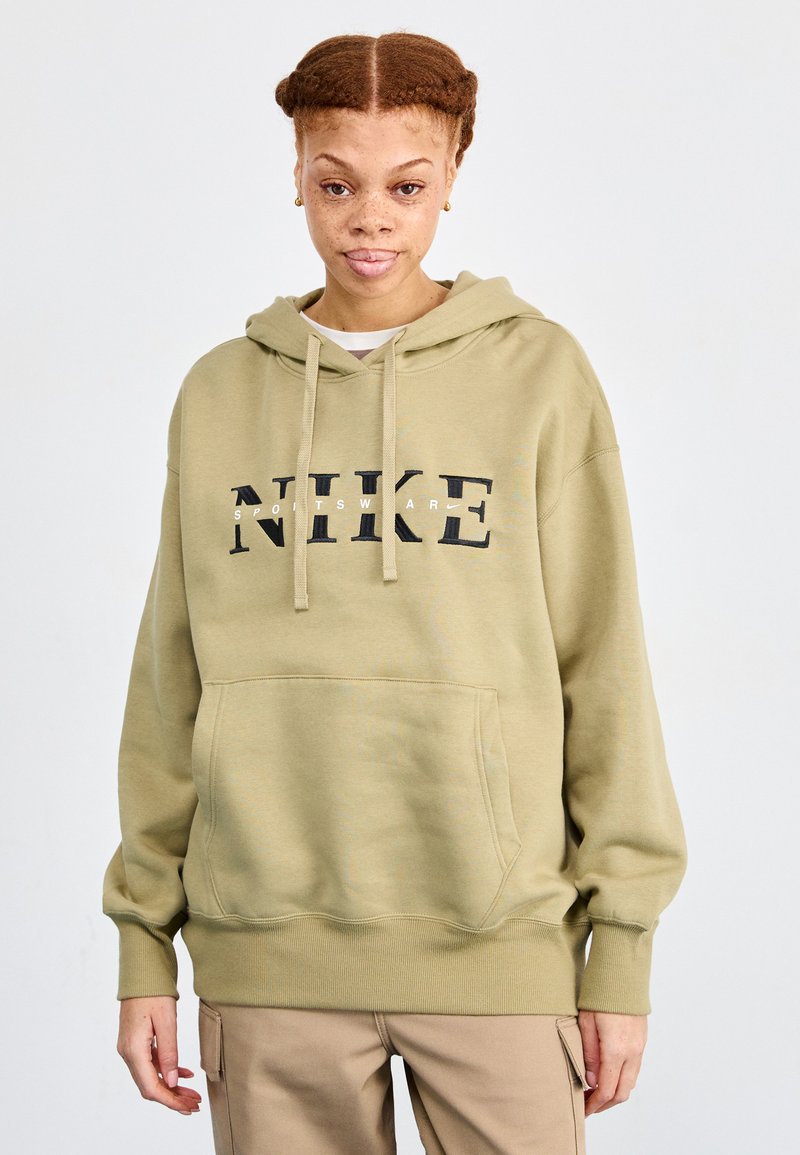 Alyvuogių žaliai spalvos džemperis su kapuce, priekine kengūrine kišenė ir juodu "NIKE SPORTSWEAR" logotipu. Minkšta, tekstūruota medžiaga su šonkaulinėmis rankovėmis.