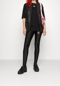 Černá kožená blazer over černým tričkem, doplněná lesklými černými legínami se bílým logem Puma a černými platformovými teniskami. Růžová taška jako akcent.