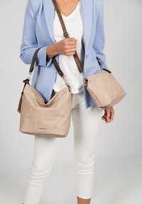 Two beige handbags made of textured material, one is a hobo style with a slouchy shape, the other a square design with a short strap detail.