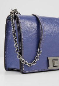 Borsa in pelle di un blu intenso con una finitura texturizzata, dotata di una tracolla in catena argentata, chiusura metallica e dettagli di cucitura in contrasto.