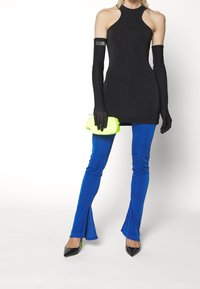 Czarna sukienka bez rękawów z wysokim dekoltem, zestawiona z niebieskimi spodniami w dzwony. Akcesoria to neonowozielona kopertówka i długie czarne rękawiczki.