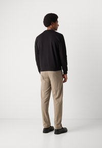 Schwarzer Pullover mit gerippten Bündchen und Saum, getragen mit beigen Hosen und schwarzem Schuhwerk, welcher ein einfaches, lässiges Design von hinten präsentiert.