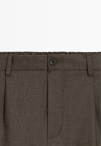 Pantalon marron foncé sur mesure avec fermeture à boutons, passants de ceinture et plis subtils sur fond blanc.