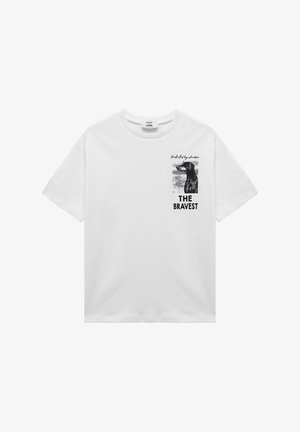 Hvid bomulds T-shirt med et sort-hvidt grafik af en hunds profil og teksten "DEN MODIGSTE" nedenunder. Korte ærmer, rund hals.