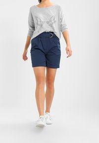 Haut à manches longues gris clair avec un motif d'étoiles, associé à un short bleu marine avec une ceinture élastique et un détail de boucle argentée.