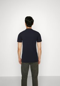 Dunkelblaues T-Shirt mit kurzen Ärmeln und Rundhalsausschnitt, taillierte Form und glatte Textur, kombiniert mit olivgrünen Hosen. Rückansicht.