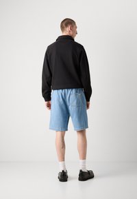 Giacca nera con cappuccio e texture a coste, abbinata a pantaloni shorts in denim azzurro chiaro con tasca posteriore. Scarpe nere e calzini bianchi completano il look.