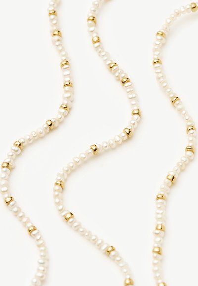 Stränge kleiner weißer Perlen, abwechselnd mit glänzenden goldenen Perlen, angeordnet in wellenförmigen Linien auf weißem Hintergrund.