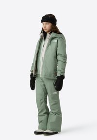 Πράσινο-μέντα χειμωνιάτικο μπουφάν και παντελόνι, συνδυασμένα με μαύρα γάντια και κορδέλα. Διαθέτει φερμουάρ και λογότυπα. Λείο, ανθεκτικό στο νερό υλικό.