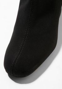 Zapato de tela negra con puntera redondeada y costura central en la parte superior, presentado sobre un fondo blanco.