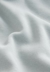 Vaaleansininen kangas, jossa on pehmeä ja teksturoitu kudonta, joka esittelee hellävaraisia poimuja ja ryppyjä. Materiaali näyttää joustavalta ja sileältä.