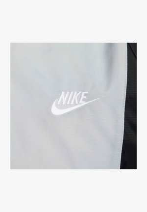 Nike-logotyp i vit brodyr på ett ljusgrått tyg med en mjuk textur. Tyget kantas av svart material.