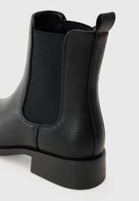 Bota Chelsea de cuero negro con panel lateral elástico, punta redonda y tacón bajo. Textura suave con detalles de costura sutiles.