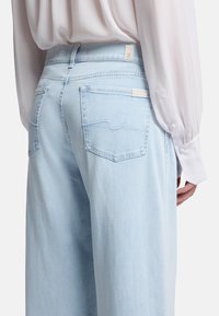 I jeans in denim blu chiaro presentano una vita alta, un taglio dritto e due tasche posteriori con sottili dettagli di cucitura. Un'etichetta è visibile sulla vita.