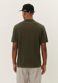 Olive green short-sleeve polo shirt with a ribbed collar, featuring a soft texture and straight hem. Paired with light striped pants.