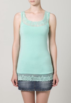 Tyrkysově zelené tílko s krajkovou lemovkou u výstřihu a okraje. Měkká tkanina, přiléhavý střih, vrstvený krajkový detail na spodní části. Stylizované s džínovou sukní.