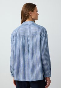 Blue and white striped long-sleeve shirt with a collar, featuring a relaxed fit and button accents on the cuffs. Soft, lightweight fabric.
