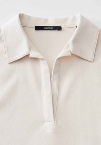 Beige Poloshirt mit weichem Stoff, klassischem Kragen, halber Knopfleiste und einem schwarzen Markenschild mit der Aufschrift "someday."