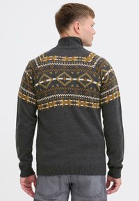 Grå strikket sweater med høj krave, prydet med et mønster i brun, creme og sennep over skuldrene og den øvre ryg.