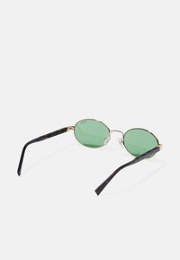 Oval sunglasses with green lenses, gold metal frame, and black tortoiseshell arms. Features clear nose pads and subtle branding on arms.