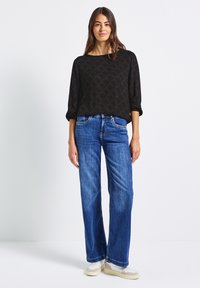 Zwarte gebloemde blouse met een ruime halslijn en driekwartmouwen, gecombineerd met lichtblauwe wijde jeans en beige sneakers.