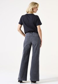 Hochtaillierte, weit geschnittene Jeans aus dunkelgrauem Denim mit zwei Gesäßtaschen und einem Reißverschluss, kombiniert mit einem schwarzen T-Shirt mit kurzen Ärmeln.