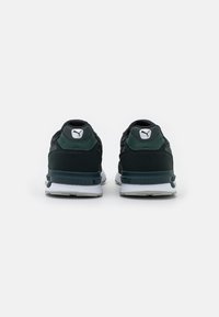 Scarpe sportive nere e verde scuro con una parte superiore testurizzata, costruzione leggera, suola bianca spessa e logo PUMA sul tallone e sulla linguetta.