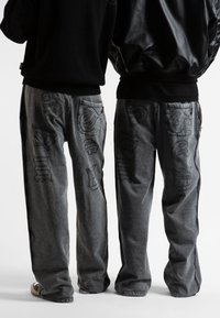 Φαρδιά γκρι τζιν παντελόνια με λεπτομερή μαύρα ραφές, διαθέτοντας διάφορα αφηρημένα σχέδια στις πίσω τσέπες και άνετη εφαρμογή.