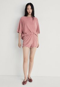 Rosa frotté oversized t-shirt och shorts set. Avslappnad passform, korta ärmar, elastisk midja, tillsammans med halkskor i liknande färg.