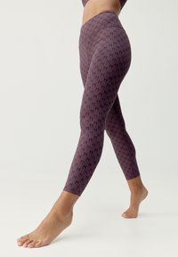 Fioletowe legginsy z powtarzającym się czarnym wzorem, z podwyższonym stanem, dopasowanym krojem zwężającym się w kostkach, wykonane z elastycznej tkaniny.
