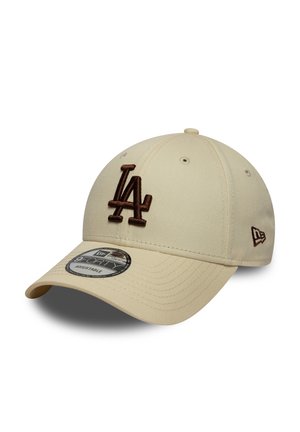 Light beige baseball cap with brown embroidered "LA" logo. Features a curved brim and a textured fabric surface. Adjustable strap at the back.