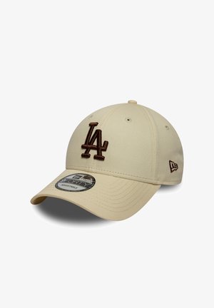 Light beige baseball cap with brown embroidered "LA" logo. Features a curved brim and a textured fabric surface. Adjustable strap at the back.
