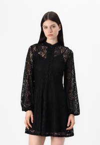 Μαύρο φόρεμα δαντέλας με μακριά φουσκωτά μανίκια, ψηλό λαιμό και λεπτομέρειες κουμπιών μπροστά. Διαθέτει περίπλοκο floral σχέδιο.