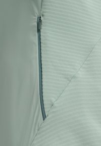 Close-up van een deels open ritssluiting op lichtgroene, gestructureerde stof met een glad stoffen paneel.