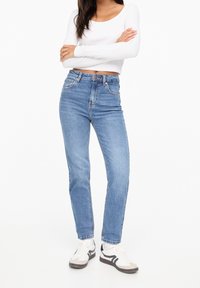 Höga blå jeans i blekt denim med fem fickor, dragkedja och raka ben, tillsammans med vita sneakers.