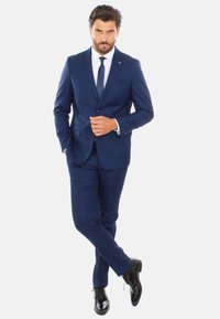 Abito blu navy con un design slim-fit, caratterizzato da rever a forma di notched e chiusura a un bottone. Accompagnato da una camicia bianca e una cravatta, scarpe nere eleganti.