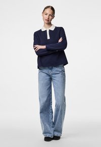 Marineblå langermet polo med hvit krage, kombinert med lyseblå vide jeans og svarte sko. Glatt stoff, avslappet passform.