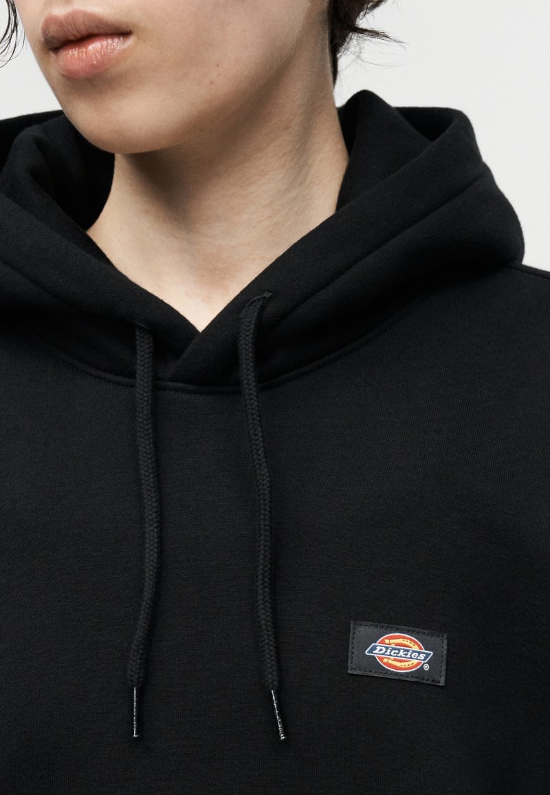 Person wearing a black Dickies hoodie with drawstrings, showing neck and lower face against a plain light background.