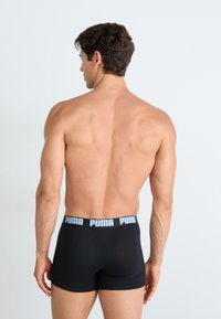 Boxeri negri dintr-un material elastic, cu un tiv moale pe care este inscripționat cu litere de culoare albastru deschis cuvântul "PUMA". Imaginea prezintă spatele boxerilor.